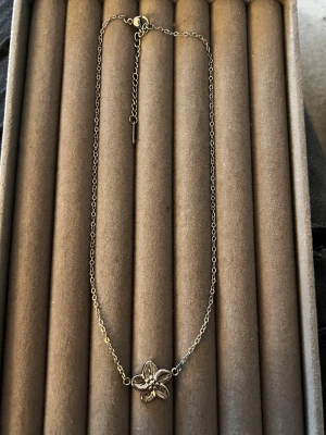 Silverhalsband med blomma - Snyggt halsband i silverfärgad metall med en detaljrik blomma i mitten. Blomman har fem blad och små pärlliknande detaljer i mitten. Kedjan är tunn och justerbar med ett enkelt lås. Perfekt accessoar för dig som gillar stilrena och feminina smycken.