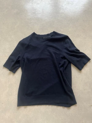 Mörkblå topp med kort ärm - En enkel och stilren mörkblå stickad topp med rund halsringning och korta ärmar. Perfekt till jeans eller kjol för en clean look. Materialet känns mjukt och följsamt mot huden.