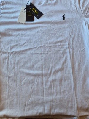 Vit t-shirt från Polo Ralph Lauren - Klassisk vit t-shirt från Polo Ralph Lauren med rund halsringning och den ikoniska loggan broderad på bröstet. Tillverkad i mjuk bomull för en skön känsla och perfekt passform. En stilren basic som funkar till allt. 