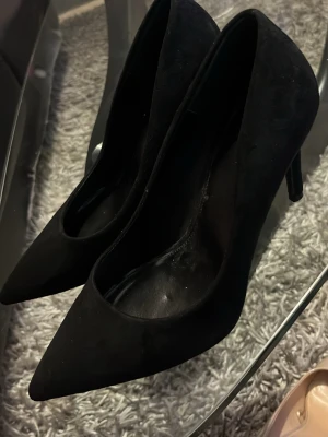 Svarta pumps från Jenny Fairy - Snygga svarta pumps från Jenny Fairy med spetsig tå och smal klack. Skorna är i mockaimitation och har en klassisk, elegant design som passar till många olika outfits. Perfekta för dig som gillar stilrena och tidlösa skor.