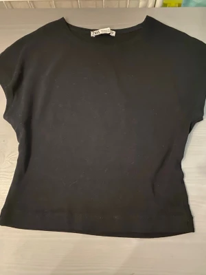 Svart topp från Zara - En enkel och stilren svart topp från Zara med rund halsringning och korta ärmar. Materialet är mjukt och stretchigt, perfekt för att matcha med jeans eller kjol. Toppens minimalistiska design gör den lätt att kombinera med olika outfits.