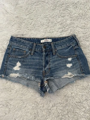 Blå lågmidjade shorts Hollister - Säljer ett par lågmidjade vintage jeansshorts från Hollister med slitna detaljer. Säljer pga för stora på mig som brukar ha S! 💞