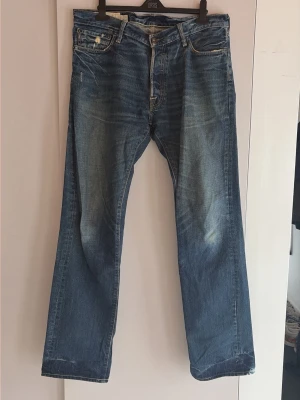 Blå raka jeans från Abercrombie & Fitch - Säljer ett par klassiska blå jeans från Abercrombie & Fitch  med raka ben och slitna detaljer. Jeansen har fem fickor, synliga nitar och en cool tvättad look. Perfekta för dig som gillar en avslappnad och tidlös stil.