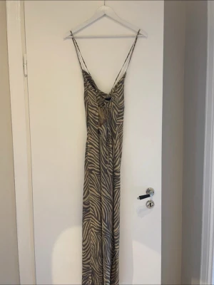 Adoore klänning  - Säljer en långklänning med zebramönster i beige och grå toner. Klänningen har smala axelband och en lös, rak passform med lätt draperad urringning. Perfekt för dig som gillar djurmönstrat och vill ha en stilren men ändå iögonfallande look.