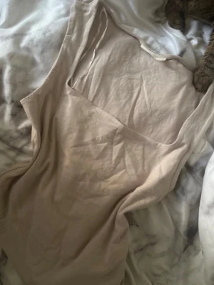 Beige ärmlös topp från Gina Tricot - Säljer en enkel och stilren beige topp från Gina Tricot, basically basics-kollektionen. Toppen är ärmlös med rund halsringning och tillverkad i mjuk bomull, perfekt för en clean och avslappnad look.