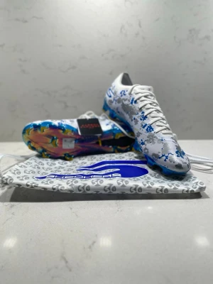 Vita Skechers fotbollsskor( limited edition)  - (Har tagit bort lappen)Säljer ett par vita Skechers fotbollsskor med blått och grått camomönster. Skorna har färgglad sula och klassisk snörning. Medföljer en matchande påse med Skechers-logga. Perfekta för dig som vill sticka ut på planen.