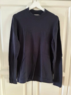Mörkblå långärmad tröja - En stilren mörkblå stickad långärmad tröja med rund halsringning. Tröjan är enkel i designen utan tryck eller mönster och passar perfekt till jeans eller chinos. Tillverkad i mjukt material som känns skönt mot huden. Storlek m men passar mer s. 