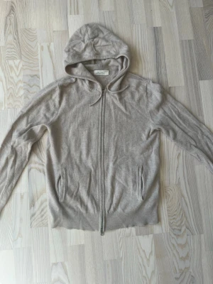 Sayless hoodie - Mysig beige hoodie i cashmere från Sayless med dragkedja framtill och två fickor. Klassisk modell med huva och ribbade muddar vid ärmslut och nederkant. Perfekt för dig som gillar stilrena och bekväma plagg.