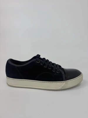 Mörkblå Lanvin sneakers med lackad tå - Snygga mörkblå sneakers med ovandel i mocka och en glansig, lackad tådel. Skorna har vita sulor och matchande mörkblå skosnören. Perfekt för dig som gillar en stilren men ändå unik look.