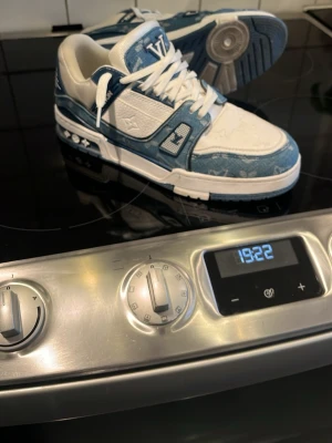 Louis Vuitton blåvita sneakers - Säljer ett par Louis Vuitton sneakers i blått och vitt med klassiskt monogrammönster. Skorna har vita snören, LV-logga på plösen och detaljer i blå denim-liknande material. Snygg kontrast mellan de olika materialen och färgerna. Perfekt för dig som vill sticka ut.