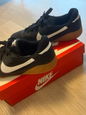 Nike svartvita sneakers med gummisula - Snygga sneakers från Nike i svart med vit swoosh och klassisk gummifärgad sula. Lågt skaft och stilren design som passar till det mesta. Ovandelen är i textil och syntetmaterial. Perfekta för dig som gillar streetwear och sportig stil.