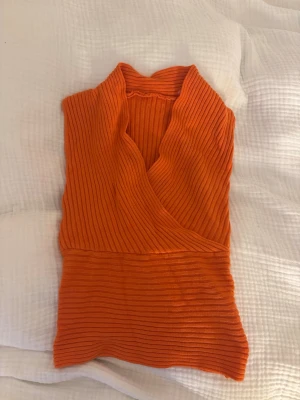 Ribbad omlottopp i orange - Trendig ribbad omlottopp i stark orange färg. Toppen är aldrig använd men köpt second hand och är i väldigt fint skick. Märket är okänt och tröjan sitter som en s
