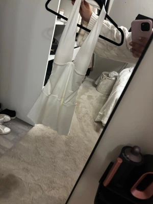 Vit kort halterneckklänning - Snygg vit kort klänning med halterneck och öppen rygg. Klänningen har en lätt utsvängd kjol och är ärmlös, perfekt för varmare dagar. Tillverkad i ett mjukt och stretchigt material som ger en bekväm passform.