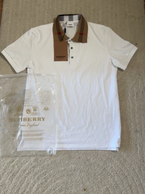 Burberry Vit pikétröja  - Vit pikétröja från Burberry med klassisk rutig krage i beige, svart och rött.