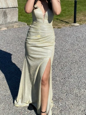 Balklänning  - Så otroligt fin balklänning i glittrande guldfärg med djup v-ringning och mesh-detalj framtill. Klänningen har en figurnära passform, drapering i midjan och hög slits på ena benet. Använd 1 gång på balen, släpet på klänningen är lite smutsigt då jag inte tvättat den sen jag använde den. Men går definitivt att tvätta bort! Annars super fint skick. Man knyter och spänner åt i ryggen! Storlek S passar säkert Xs också eftersom man spänner själv! Nypris 3000kr säljer direkt för 1999! 😍💞