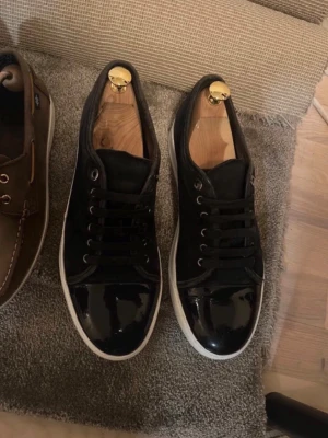 Lanvin Navy - Snygga svarta sneakers med glansiga lackdetaljer på tån och klassisk vit sula. Skorna har svarta skosnören och metallhål för snörningen. Perfekta för dig som vill ha en stilren men ändå iögonfallande look till vardagsoutfiten.