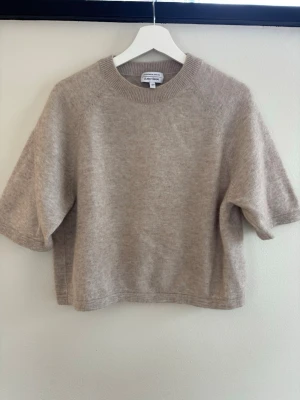 Beige stickad tröja & Other Stories - Kortärmad beige stickad tröja från & Other Stories Stockholm Atelier. Tröjan har rund halsringning och är gjord i ett mjukt, fluffigt material som ger en avslappnad och trendig look. Perfekt att styla med jeans eller kjol för en chill vibe.