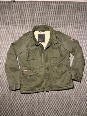 Grön fieldjacket - Tja! Säljer denna snygga fieldjacket från superdry! Storlek i jackan är L. Men den passar som M. Om du är osäker på om den passar kan jag skicka mått