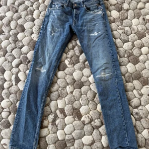 Blå slitna jeans från Replay - Säljer ett par blå jeans från Replay med raka ben och slitna detaljer på lår och knän. Klassisk femficksmodell i denim med snygg tvätt.I fint skick men en hälla är trasig, se bild.
