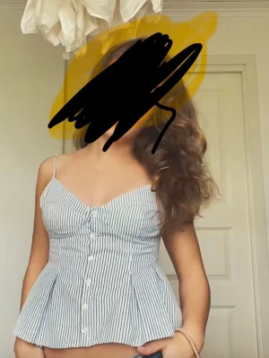 Somrig topp Zara - Säljer en söt peplumtop med tunna axelband och knappar framtill. Toppen har smala blå och vita ränder, v-ringning och figurnära passform upptill som går ut i en volang nedtill. Perfekt till jeans eller kjol för en fräsch sommarlook.