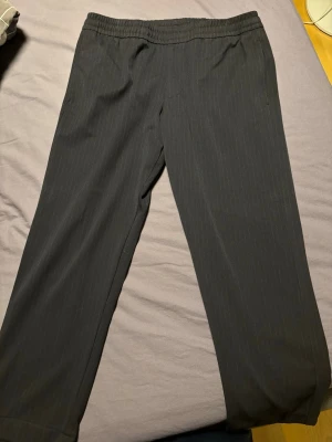 Mörkblå relaxed byxa med resår - Säljer ett par helt nya mörkblå randiga byxor med relaxed fit och resår i midjan. Byxorna har raka ben och är tillverkade i ett mjukt tyg som känns bekvämt. 