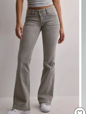 Grå bootcut jeans med fickdetaljer - Snygga grå bootcut jeans med låg midja och dubbla knappar framtill. Jeansen har dekorativa fickor bak med lock och knapp, samt klassiska fickor fram. Tillverkade i stretchigt denim för skön passform. Original pris 699kr. Använt några gånger och tvättade 1 gång därför ser dom väldigt små ut