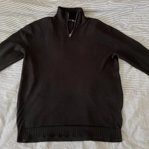 Svart halvzip tröja från 157 - Svart långärmad tröja från 157 med halv dragkedja och hög krage. Tröjan har ribbade muddar vid ärmslut och nederkant. Perfekt för lager-på-lager och enkel att matcha med olika outfits.