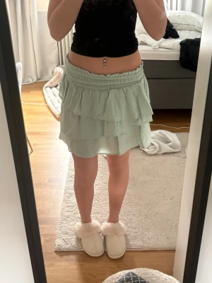 Ljusgrön volangkjol med resårmidja - Söt ljusgrön kortkjol med dubbla volanger och bred resår i midjan. Kjolen har en luftig och flowy känsla, perfekt för varmare dagar. Ingen synlig logga eller märke.