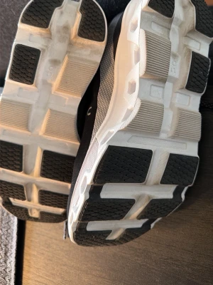 Svarta löparskor från On Running - Säljer ett par svarta löparskor från On Running med vit och svart sula. Skorna har ventilerande meshmaterial, snörning och den ikoniska CloudTec-sulan för extra dämpning. Perfekta för dig som vill ha snygga och tekniska träningsskor. Modell cloudmonster