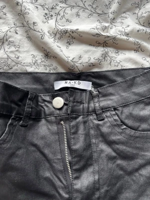 Svarta jeans från NA-KD - Säljer ett par svarta jeans från NA-KD som är med utsvängda ben med hög midja. Materialet har en glansig utsida nästan som om det vore läder, dock tror jag inte att det är läder. Lappen som ni ser på bilden har lossnat. Det fram kommer inte vilken storlek men jag som är 160 och har storlek 34 på jeans kan ha dessa. Näsan aldrig använda då jag inte är nått för sånna. 