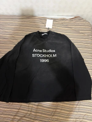 Acne studios longsleeve - Cool svart sweatshirt från Acne Studios med vit text 'STOCKHOLM 1996' på bröstet. Tröjan har rund hals och långa ärmar. Materialet är mjukt och bekvämt, perfekt för en avslappnad look. Märkeslapp och tagg sitter kvar.