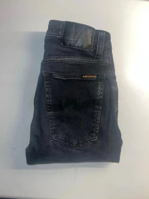 Nudie jeans  - Säljer ett par svarta skinny jeans från Nudie Jeans. Materialet är mjukt denim med stretch för extra komfort. Midja 31cm, längd 104cm. JAG SKICKAR EJ FLER BILDER NÄR JAG BÄR JEANSEN! för storleksguide hänvisar jag till måtten och för bättre inblick i passformen rekommenderar jag att googla på modellnamnet. kolla måtten noggrant :) s5,1.         