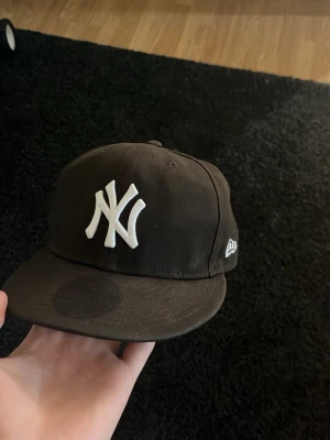 Svart New Era Yankees keps - Snygg svart keps från New Era med klassiskt New York Yankees broderat vitt logotyp framtill. Kepsen har rak skärm och broderade ventilationshål. Materialet är bomull och modellen är fitted utan justering bak.