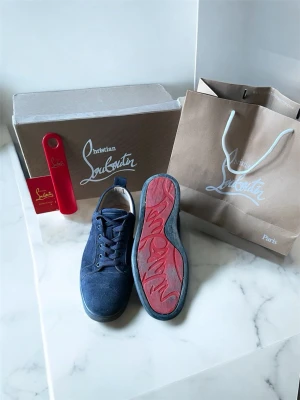Marinblå sneakers från Louboutin - Snygga marinblå sneakers från Christian Louboutin i mocka med klassisk röd sula och diskreta detaljer. Lågt skaft och rundad tå ger en clean look. Perfekta för dig som vill ha något exklusivt och stilrent i garderoben.