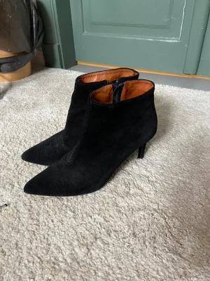 Svarta mocka stövletter med klack - Snygga svarta stövletter i mocka med spetsig tå och smal klack. Dragkedja på insidan och brunt foder i läder Perfekta för dig som gillar en stilren och trendig look. Passar perfekt att ha till ett par jeans eller liknande😍