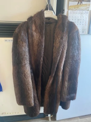 Brun pälsjacka med huva - Säljer en brun mink pälsjacka med huva i klassisk modell. Jackan har en lyxig look med glansig päls och helfoder på insidan. Perfekt för dig som vill ha en varm och snygg jacka till vintern. Stängs framtill och har en avslappnad passform.