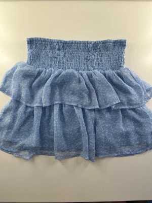 Blå volangkjol med blommönster från vero moda💙 - Söt blå kortkjol med volanger och små vita blommor. Kjolen har en bred smock i midjan för skön passform och är gjord i ett lätt, luftigt material som passar perfekt till varma dagar. Jag har använt den som som både strapless top och kjol!