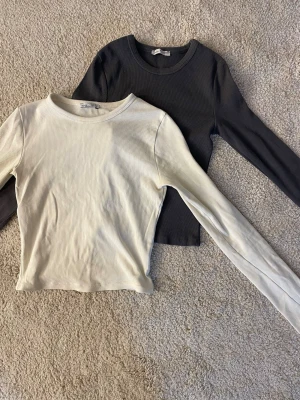 Ribbade långärmade toppar i mörkgrått och créme vit - Två stilrena ribbade långärmade toppar i grått och vitt. Båda har rund halsringning och i storlek XS från Bershka. Säljer dom även individuellt 🤍🩶