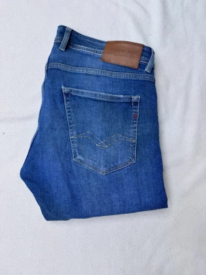 Blå jeans från Replay  - Snygga blå jeans från Replay med klassisk femficksmodell och skinnpatch bak i midjan. Jeansen har raka ben och diskreta slitningar framtill för en avslappnad look. Tillverkade i mjuk denim som sitter skönt hela dagen.