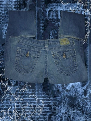 Blå bootcut low waist jeans från True Religion - Säljer ett par blå bootcut jeans från True Religion med ikoniska kontrastsömmar och stora fickor bak med knappar. Jeansen har en klassisk femficksmodell och är tillverkade i slitstarkt denim. Perfekta för dig som gillar en avslappnad men snygg stil.