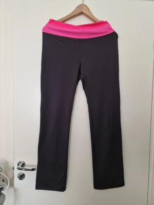 Mörkgrå leggings med rosa midja - Säljer ett par mörkgrå leggings med bred, dubbelvikt midja i starkt rosa nyans. Modellen har raka ben och är tillverkad i stretchigt material som sitter skönt. Perfekta för träning eller chill. Inget synligt märke. H&M i storlek M. Elastiska. 