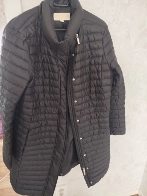 Svart dunjacka från Michael Kors - Snygg svart dunjacka från Michael Kors med quiltat mönster och hög krage. Jackan har dragkedja och tryckknappar framtill samt diskreta fickor på sidorna. Perfekt för kalla vinterdagar och ger en stilren look.pris ny 2000kr mitt pris 500 kr använder mig av Postnord storl L 