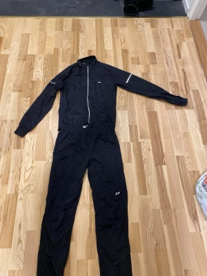 Svart träningsset - Säljer ett svart träningsset, perfekt för löpning eller annan utomhusträning. Setet består av en jacka med hel dragkedja, reflexdetaljer på ärmarna samt matchande byxor.