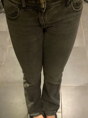 Grå bootcut jeans med fickdetaljer - Säljer ett par grå bootcut jeans med snygga fickdetaljer bak och dubbla knappar fram. Jeansen har en lätt tvättad look och är tillverkade i ett mjukt denimtyg som sitter skönt. Perfekta för dig som gillar en avslappnad men trendig stil.