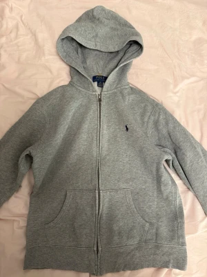 Grå hoodie från Polo Ralph Lauren - Snygg grå hoodie från Polo Ralph Lauren med dragkedja framtill och klassisk huva. Storlek 14-16 år.