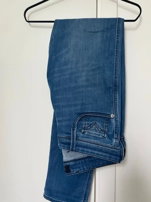 Blå jeans från Replay - Snygga blå jeans från Replay med klassisk femficksmodell och diskret slitning på låren. Jeansen har detaljerad söm på bakfickan. Tillverkade i mjuk denim med en skön passform. Modellen är Anbass.