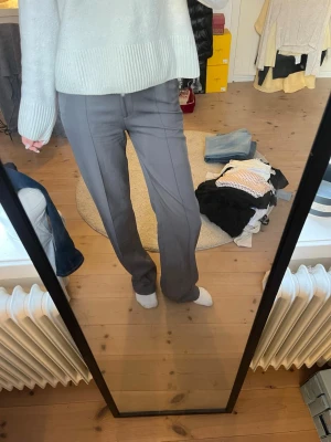 Grå kostymbyxor med raka ben - Snygga grå kostymbyxor med raka ben och pressveck. Byxorna har hög midja och klassisk passform, perfekta till en stilren look. Materialet ser ut att vara en mjuk och lite stretchig blandning, vilket gör dem bekväma att bära hela dagen.