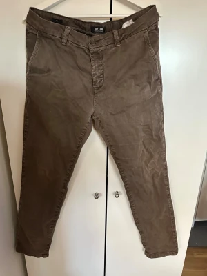 Bruna chinos från Only & Sons - Snygga bruna chinos från Only & Sons med klassisk rak passform. Byxorna har framfickor, bälteshällor och två bakfickor med knapp. Tillverkade i mjukt bomullsmaterial som ger en avslappnad men stilren look. Storlek W32 L32