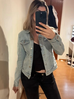 Ljusblå  jeansjacka - Snygg ljusblå jeansjacka med raka sömmar och silverfärgade knappar. Jackan har två bröstfickor med lock och knapp, samt klassisk krage. 