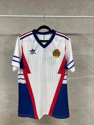 Adidas fotbollströja Jugoslavien - Retro fotbollströja från Adidas i vitt med blå och röda blixtdetaljer, blå V-ringad krage och ärmslut. Tryck med Jugoslaviens landslagsmärke på bröstet och Mihajlović 11 på ryggen. Perfekt för dig som gillar klassiska fotbollströjor. Finns i olika storlekar!!! Pris kan diskuteras!!!